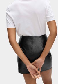 Bílá tričko s krátkým rukávem v kombinaci s černou mini sukní z umělé kůže. Sukně má úzký pas a hladkou, lesklou texturu.