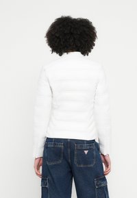 Fehér bélelt dzseki magas gallérral, texturált felülettel és varrási részletekkel, kék cargo nadrág fölött, hátul zsebekkel.