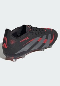 Black soccer cleat with red and gray accents, textured synthetic upper, six transparent studs, and bold branding on the side.