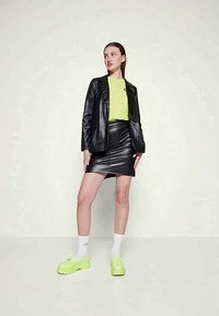 Μαύρο δερμάτινο σακάκι πάνω από ένα φωτεινό πράσινο T-shirt, συνδυασμένο με μαύρη δερμάτινη φούστα mini και νεον πράσινα αθλητικά παπούτσια με λευκές κάλτσες.