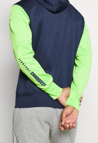 Hooded sweatshirt with a navy body and vibrant green sleeves. Features "SEAHWKS FOOTBALL" printed along the left sleeve.