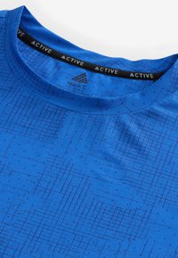 Blå træningsshirt med et struktureret mønster af krydsende linjer, rund hals og et sort mærke med "NEXT ACTIVE" branding.