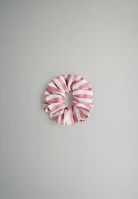 Coletero de tela a rayas rosa y blancas sobre un fondo liso gris claro, visto desde arriba.