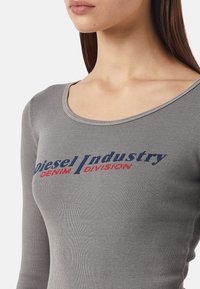 Haut à longues manches gris côtelé avec un décolleté en scoop, arborant un texte bleu et rouge contrasté portant les mots "Diesel Industry Denim Division."
