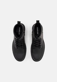 Botas de tobillo de cuero negro con cierre de cordones, acabado suave y una lengüeta en la parte trasera para facilitar su uso.