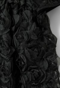 Crna tkanina s višeslojnim, teksturiranim cvjetnim aplikacijama koje nalikuju ružama. Dizajn ima prozirni sloj s mekim, lepršavim izgledom.