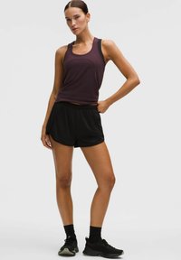 Bordeaux tanktop, zwarte sportshorts en zwarte sneakers. De outfit heeft een strakke pasvorm met een relaxte fit bij de shorts.