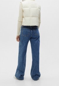 Weißer Puffer-Weste, tailliert hinten, kombiniert mit lockeren blauen Jeans aus Denim mit fünf Taschen und einem ausgeblichenen Finish. Strukturiertes Material, entspannte Passform.