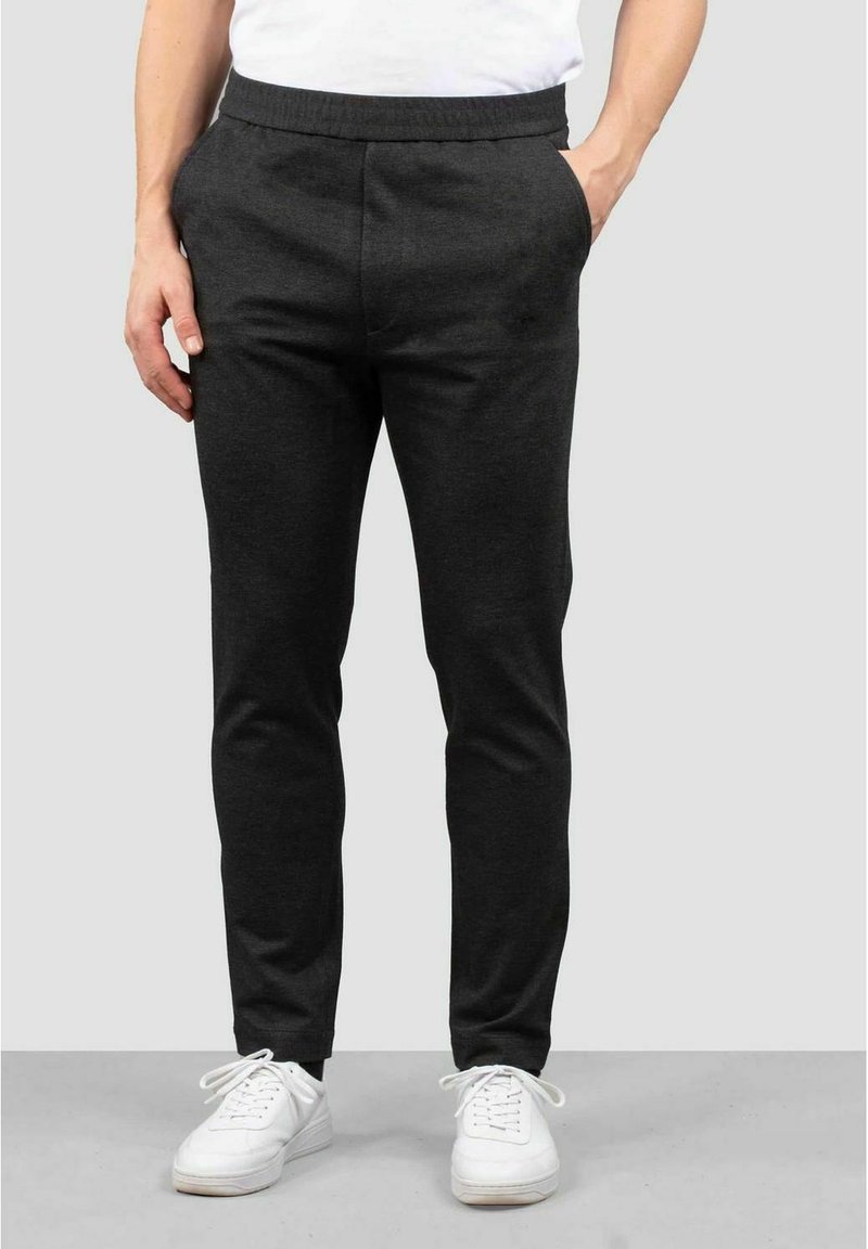 Herrars mörkgrå joggerbyxor med elastiskt midjeband och sidofickor, tillverkade av ett mjukt, texturerat tyg. Matchat med vita sneakers.