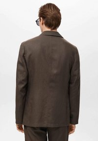 Brązowa kurtka o dopasowanym kroju, z klapami z wycięciem, gładką fakturą i czystymi liniami, noszona z dopasowanymi spodniami.