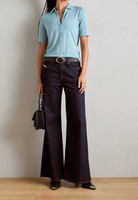Polo blu chiaro a maniche corte, jeans a gamba larga scuri, cintura nera con fibbia argentata e piccola borsa nera a trama.