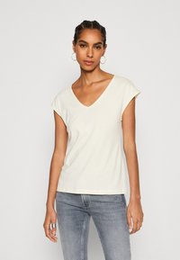 Crème-kleurig t-shirt met een v-hals, korte opgerolde mouwen en een relaxte pasvorm, gemaakt van zachte stof die geschikt is voor casual gebruik.
