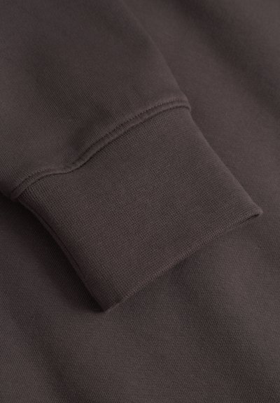 Manche de sweat-shirt marron foncé avec un poignet côtelé, montrant une texture de tissu en maille fine et des détails de couture soignés.