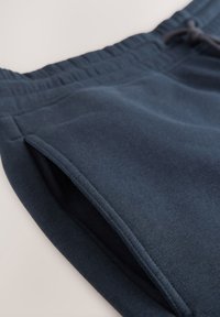 Pantalon de survêtement bleu marine avec une taille élastique et une poche latérale sur un fond clair.