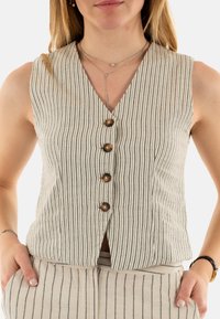 Chaleco a rayas beige con escote en V, que cuenta con cuatro botones y un corte ajustado. La tela tiene una textura suave. Combinado con pantalones a rayas.