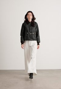 Jachetă bomber neagră, matlasată, cu butoane aurii, două buzunare frontale și guler maro, asortată cu pantaloni albi cu pantaloni largi și cizme negre până la gleznă.