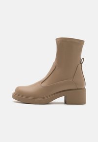 Bottine tan avec un bout rond, des panneaux élastiques sur les côtés et un talon bloc moyen. Texture lisse et détails de couture au niveau du col.