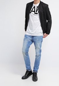 Černá bomber bunda, bílý grafický tričko, světlé modré roztrhané džíny a černé tenisky, vystihující moderní neformální styl a textury.