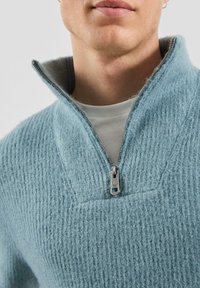 Jasnoniebieski, teksturowany sweter z kołnierzem na zamek błyskawiczny. Charakteryzuje się prążkowanym wzorem i częściowym zamkiem przy szyi. Wygląda na miękki i przytulny.