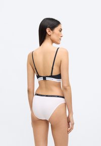 Ciemnoszary biustonosz typu bralette z regulowanymi ramiączkami i paskiem z logo; białe, wysokie majtki z czarnym paskiem z logo, gładka faktura tkaniny.