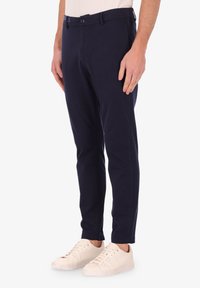 Pantaloni in cotone blu navy con vestibilità slim, tasche laterali e davanti piatto. Abbinati a sneakers bianche. Texture liscia, dettagli minimali.
