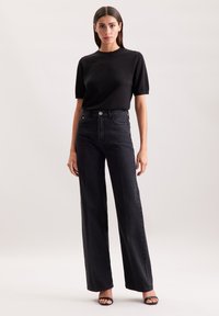 Czarna dopasowana bluzka z krótkim rękawem w połączeniu z czarnymi dżinsami o wysokim stanie i szerokich nogawkach. Ubranie ma teksturowany materiał i minimalne detale.