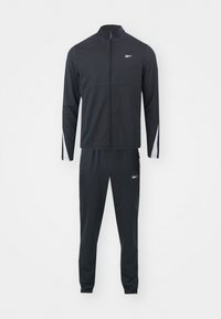 Veste de sport noire zippée intégrale avec col et pantalon de survêtement noir assorti, tous deux ornés de petits logos blancs Reebok et de détails de bandes blanches sur les manches.