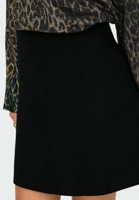 Kobieta nosząca czarną spódnicę na wysokim stanie w połączeniu z długim rękawem w panterkę, odsłaniająca część swojej ręki z pierścionkiem.