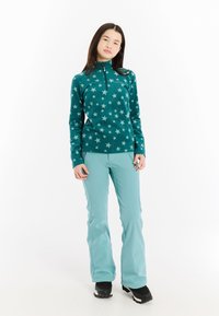 Suéter de felpa en verde azulado con patrón de estrellas blancas, cuello de media cremallera; combinado con pantalones aqua y botas negras, todo en un estilo minimalista.