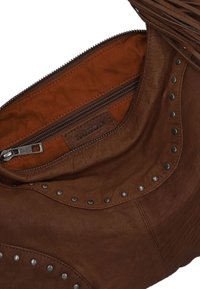 Sac à main en cuir marron avec des clous en métal à l'extérieur, une poche zippée et une finition texturée. L'intérieur présente une doublure en tissu orange contrastant.