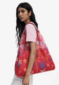 Rote Netztragetasche mit bunten Blumen- und Seesternmustern, ausgestattet mit doppelten Trägern und einem geräumigen Innenraum. Ideal für den täglichen Gebrauch.