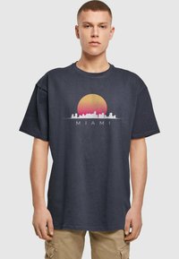Marineblå bomull T-skjorte med grafikk av en solnedgang og Miami skyline i hvitt og rosa, med ordet "MIAMI" under designet.