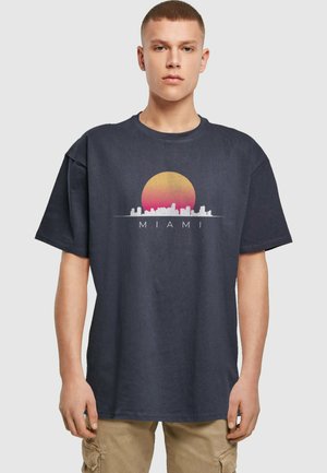 Marineblå bomull T-skjorte med grafikk av en solnedgang og Miami skyline i hvitt og rosa, med ordet "MIAMI" under designet.