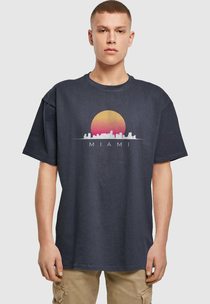 Námořnická modrá bavlněná tričko s grafikou západu slunce a siluetou Miami v bílé a růžové barvě, s nápisem "MIAMI" pod designem.