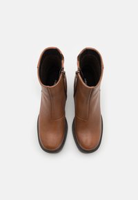 Botas de tobillo de cuero marrón con una textura suave, detalle de cremallera en el lateral y diseño de punta redonda. Forma simple y aerodinámica.