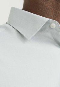 Camicia collare azzurro chiaro in tessuto strutturato, con un dettaglio a bottone sul colletto e una finitura liscia.