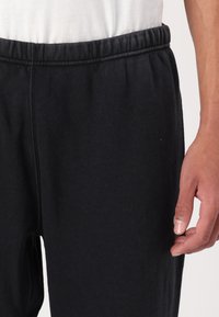 Black sweatpants made of soft cotton, featuring an elastic waistband and a slim fit design, with visible stitching details.
