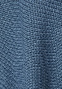 Dzianina w średnim odcieniu niebieskiego, charakteryzująca się teksturowanym, otwartym splotem oraz miękką, lekko puszystą powierzchnią.