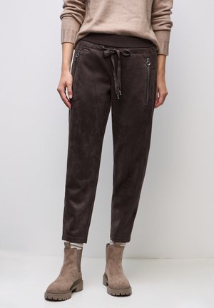 Pantalon en suède marron avec une taille à cordon, poches zippées sur les côtés et une coupe fuselée, associé à des bottines neutres.
