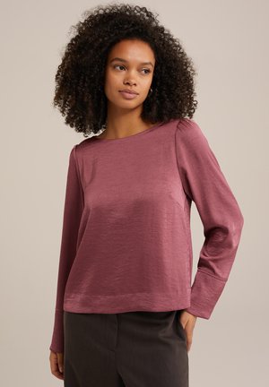 Long-sleeved top in a crinkled, soft mauve fabric. Features a wide neckline and subtle pleats at the shoulders. Paired with dark trousers.