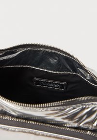 Metallic silver pouch made of smooth material with a black fabric interior. Features a zip closure and a small logo tag inside.
