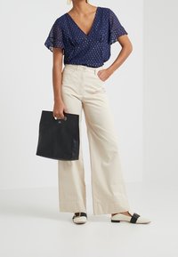 Blusa azzurra a pois con maniche a volant, pantaloni a vita alta beige a gamba larga, borsa a tracolla nera e scarpe slip-on a fantasia.