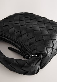 Sac en cuir noir avec un design tissé, fermeture éclair et poignée tressée. Surface texturée avec des accents en métal argenté brillant.