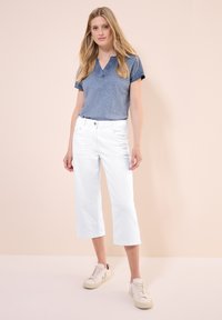 Blå kortärmad blus med V-ringning, parat med vita capribyxor och ljusa sneakers. Slätt tyg och avslappnad passform.