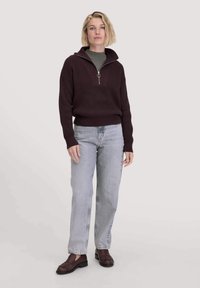 Burgunderfarbener Strickpullover mit hohem Kragen und halbem Reißverschluss, kombiniert mit hellgrauen geraden Jeans und dunklen Slipschuhen.