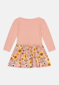 Šaty s dlouhým rukávem, které mají meruňkový žebrovaný vršek a sukni s květinovým vzorem, na které jsou slunečnice a různé květiny v odstínech růžové a žluté.