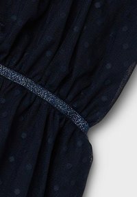 Abito navy a pois realizzato in materiale trasparente, con vita arricciata e un dettaglio in vita metallico testurizzato e scintillante.