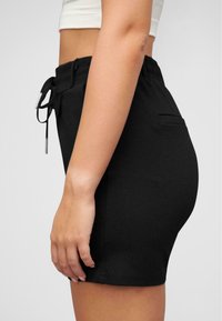 Svarte shorts med elastisk midje og snor, med en sidelomme og en slank, tettsittende design. Glatt tekstur med minimalt med detaljer.