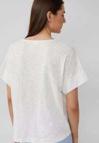 Witte top met korte mouwen en een gestructureerde afwerking, brede halslijn en een relaxte pasvorm, met opgerolde mouwen en een subtiel gestreept patroon.