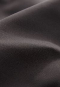 Sima, sötétszürke szövet lágy redőkkel és finom textúrával, amely diffúz fényben látható.